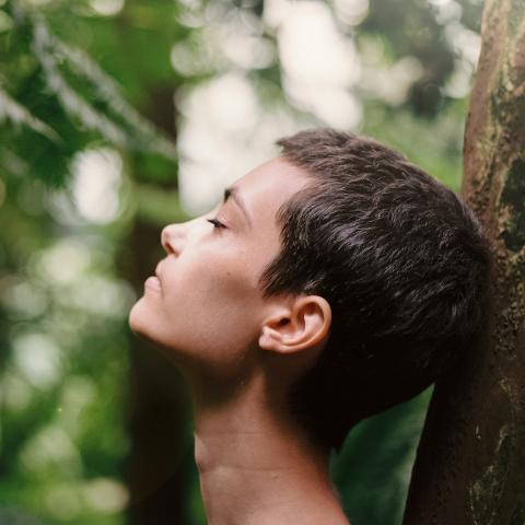 Person in the woods eyes closed with head against a tree