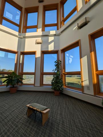 a meditation bench in a room with lots of windows overlooking a marsh on beautiful sunny day