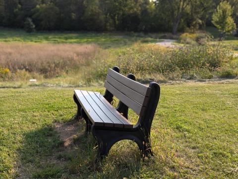 A grey bench in grass with trees off in the distance