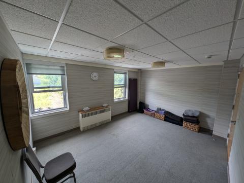 A small room with two windows, a chair, and other yoga props