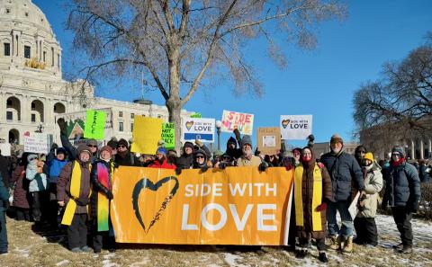 lots of unitarians standing behind a side with love sign in front of the mn capitol