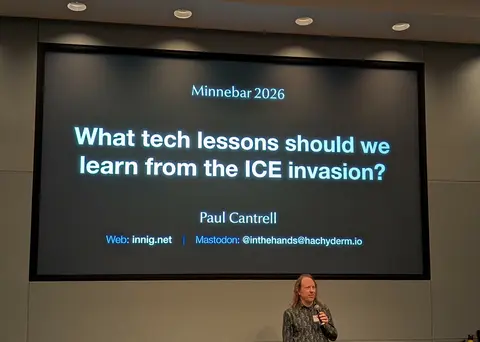 A white masc person holding a microphone stands in front of a large projector screen. The screen says:  Minnebar 2026  What tech lessons should we learn from the ICE invasion?  Paul Cantrell  Web: innig.net Mastodon: @inthehands