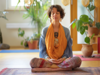 Woman sitted cross legged wearing an orange scarf seated in meditation