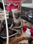 A small Buddha status surround by cables, boxes, and other little gadgets