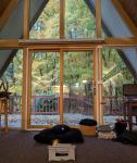 A meditation cushion on the floor in an a-frame building with fall leaves in the background visible through a large window