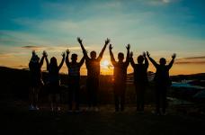 people standing outside at sunset with their arms raised