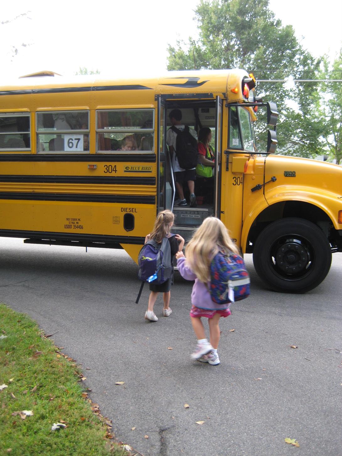 2 young kids getting on a yellow bus