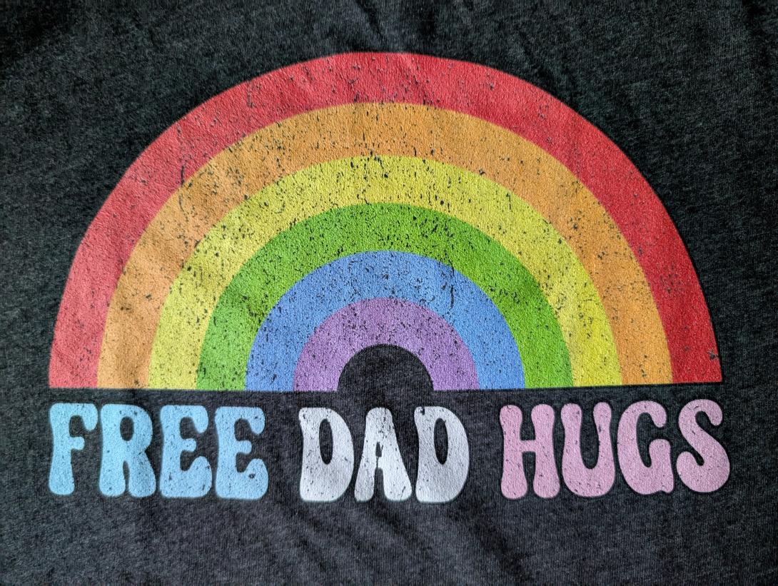 the text free dad hugs under a rainbow on a gray background