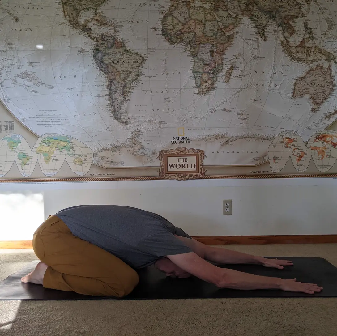 matthew doing child's pose in front of a world map