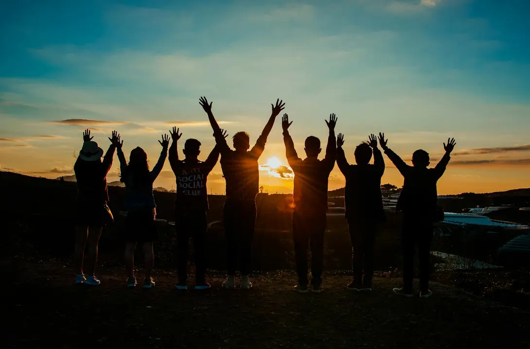people standing outside at sunset with their arms raised